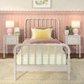 Pastel pink children's bedroom with white spindle bed, scalloped wall trim, yellow gingham bedding, matching bedside tables with heart-pattern lamps, pink alarm clock and plush frog toy