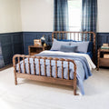 Cozy modern farmhouse bedroom with wooden spindle bed, blue quilted bedding, navy wainscoting, plaid curtains and a nightstand with lamp.