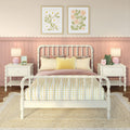 Pastel pink kids' bedroom with white spindle bed, yellow gingham pillows, floral wall art and bedside lamps.