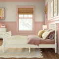Cozy pastel pink girls bedroom with white spindle bed, yellow gingham bedding and pillows, woven rug, Roman shade and scalloped wainscoting