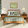 Cozy child-friendly bedroom with wooden spindle bed, green bedding and pillows, striped wallpaper, framed art, bedside tables with lamps, stacked books and teddy bear