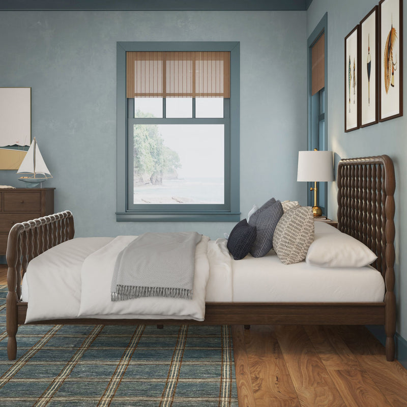 Coastal bedroom interior with wooden woven headboard, white linens, gray throw, navy pillows, sailboat decor, framed feather art and ocean-view window