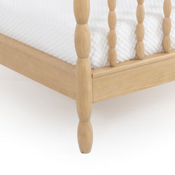 Light natural wood spindle bed frame close-up showing turned leg, side rail and white quilted mattress corner