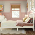 Pastel pink girls' bedroom with white spindle bed, yellow gingham bedding, velvet throw pillows, roman window shade and botanical wall art