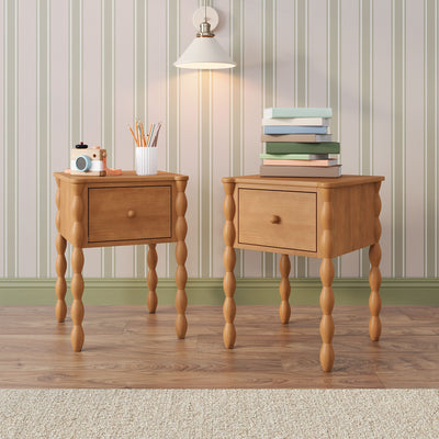 Two wooden bedside tables with turned legs against beige striped wallpaper, illuminated white wall sconce, stack of pastel books, ribbed pencil holder with colored pencils and a wooden toy camera — cozy children's room decor