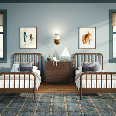 Nautical twin kids bedroom with wooden spindle beds, sailboat model, octopus plush, blue plaid rug, framed fish art and brass wall sconce