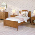 Cozy girl's bedroom interior with wooden twin bed, pink bedding and throw, floral wallpaper, wooden nightstand and dresser, round mirror, lamps and teddy bear