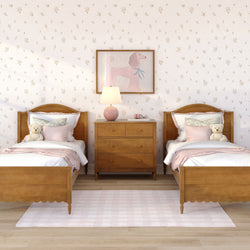 Kids' twin bedroom with wooden beds and pink bedding, teddy bears on each bed, wooden dresser with lamp, pink poodle wall art and floral wallpaper