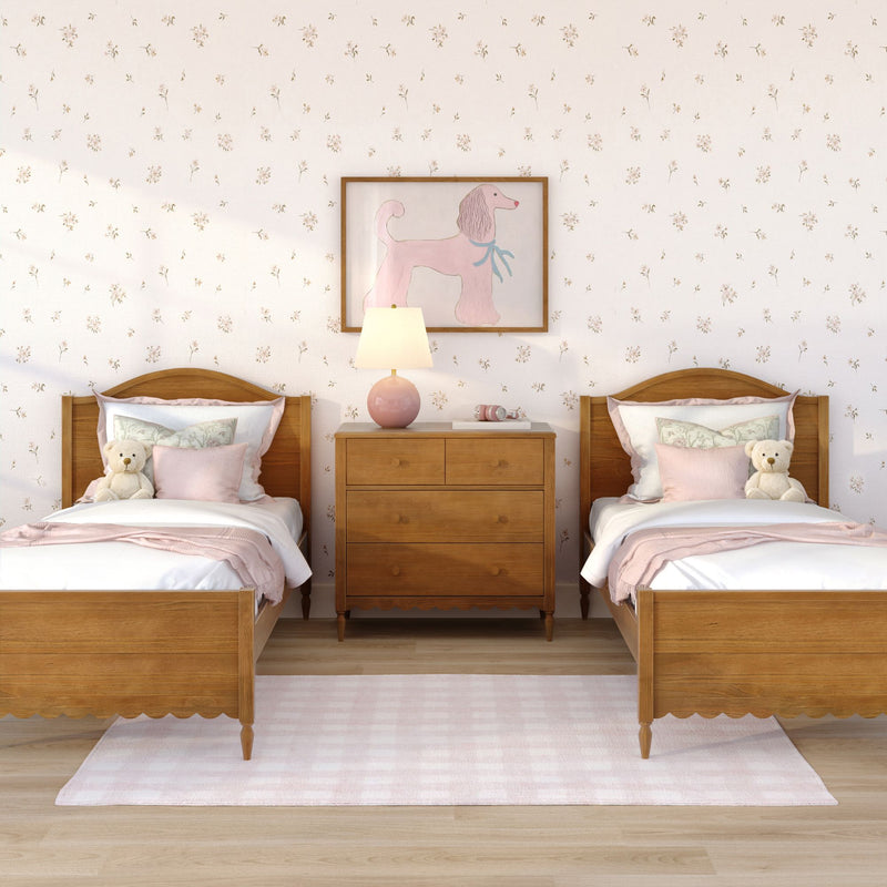 Kids' twin bedroom with wooden beds and pink bedding, teddy bears on each bed, wooden dresser with lamp, pink poodle wall art and floral wallpaper