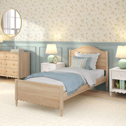 Cozy cottage-style bedroom with light wooden twin bed and scalloped headboard, pastel blue throw and floral pillows, floral wallpaper, matching nightstands, table lamps and dresser