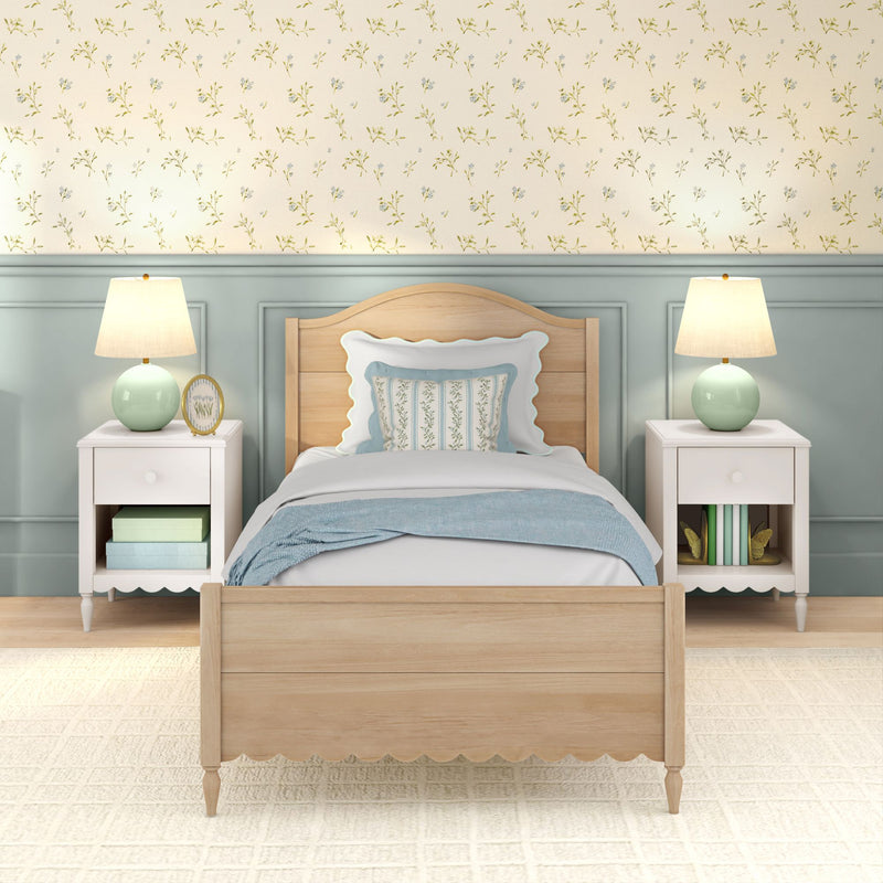 Twin coastal farmhouse bedroom with light wood scalloped bed, pastel blue bedding and decorative floral pillow, white nightstands, mint green lamps and floral wallpaper
