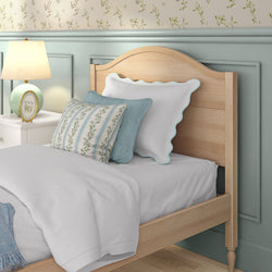 Cozy cottage-style twin bed with wooden headboard, white bedding, floral and striped decorative pillows, teal wainscoting and bedside lamp