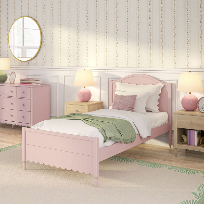 Pastel pink girl's bedroom with scalloped twin bed, green throw, pink bedside lamps, pink dresser, round mirror and floral striped wallpaper