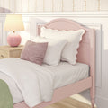 Pastel pink girls' bedroom with scalloped pink headboard, white linens and blush pillows, pink ceramic bedside lamp on a wooden nightstand and floral wallpaper — cozy vintage nursery decor