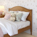 Cozy pink bedroom with wooden bed frame, white bedding, floral decorative pillows and a plush teddy bear on the bed