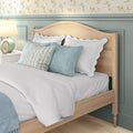 Light wood bed frame with white duvet, blue and floral decorative pillows, mint-green wainscoting and bedside lamp, cozy coastal farmhouse bedroom decor