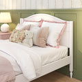 Cozy feminine bedroom with white wooden bed, soft white bedding, pink ruffled pillows, floral throw pillow, plush teddy bear, green wainscoting and bedside lamp