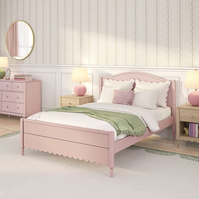 Pastel pink girls' bedroom interior with scalloped headboard bed, white pillows and green throw blanket, wooden nightstand with pink lamp, pink dresser stacked with books and round mirror, and floral striped wallpaper — feminine kids' room decor