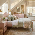 Sunlit pastel pink cottagecore bedroom with gingham bedding, floral quilt, plush throw pillows, window seat, rattan accents and bunny decor