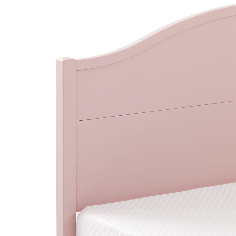 Close-up of blush pink wooden headboard with curved top on a twin bed frame and white quilted mattress, modern kids bedroom decor