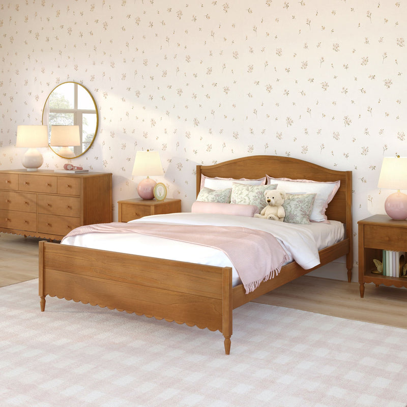 Cozy children's bedroom with wooden bed, floral wallpaper, pink bedding, bedside tables with lamps, dresser and round mirror.
