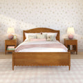 Pastel bedroom with wooden bed frame, pink floral bedding and pillows, teddy bear on bed, wooden nightstands with pink lamps and floral wallpaper