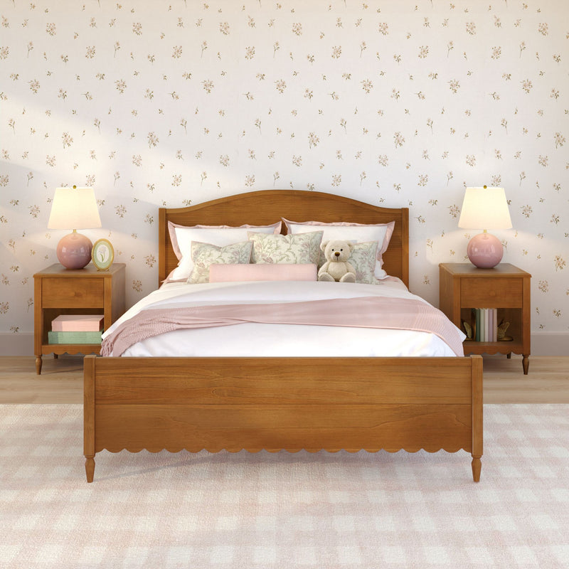 Pastel bedroom with wooden bed frame, pink floral bedding and pillows, teddy bear on bed, wooden nightstands with pink lamps and floral wallpaper