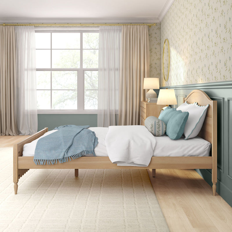 Bright cozy farmhouse bedroom with light wood bed, teal throw blanket and pillows, cream curtains, floral wallpaper, bedside lamps and natural window light