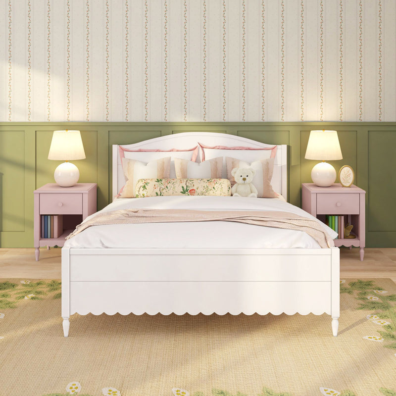 Cozy cottage-style children's bedroom with white scalloped bed, pink nightstands, floral bolster pillow, teddy bear, green wainscoting and floral wallpaper