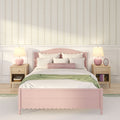 Pastel pink bedroom with scalloped pink bed frame, white bedding and pillows, green throw blanket, floral striped wallpaper, wooden nightstands and pink table lamps