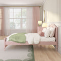 Pastel pink bedroom interior with pink wooden bed, white bedding and green throw blanket, round bolster pillow, pink nightstand with bedside lamps, large window with sheer pink curtains, oval wall mirror and green-accented patterned rug