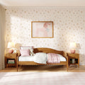 Pink girls' bedroom with wooden bed, floral wallpaper, framed poodle wall art, pastel pillows and throw, teddy bear and bedside lamps