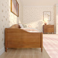Girls' bedroom interior with wooden bed and dresser, pastel pink bedding, floral wallpaper, framed art and bedside lamp