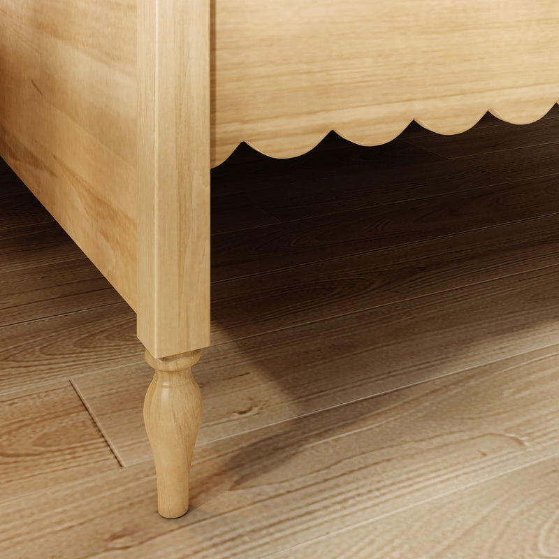 Close-up of light wood bed frame with scalloped bed skirt and turned leg on dark hardwood floor