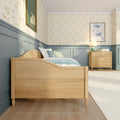 Cozy children's bedroom with light wood bed and dresser, pastel blue wainscoting, floral wallpaper, soft bedding and bedside lamp