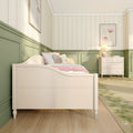 Girls bedroom nursery with cream wooden bed, pink bedding and teddy bear, pastel green wainscoting, floral wallpaper, and white dresser with lamp