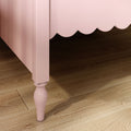 Close-up of pink scalloped bed skirt and turned bed leg on dark hardwood floor — nursery bedroom decor