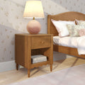 Wooden nightstand with pink ceramic bedside lamp, floral throw pillows and cream floral wallpaper in a cozy bedroom
