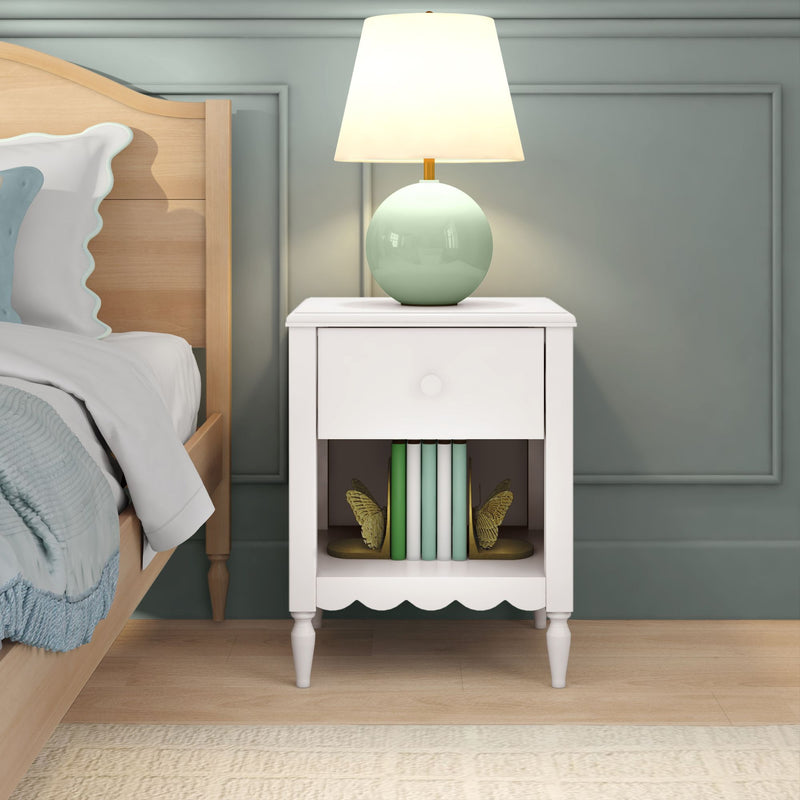 White bedside table with mint green ceramic lamp, stacked pastel books and gold butterfly bookends next to light wood bed in sage green bedroom