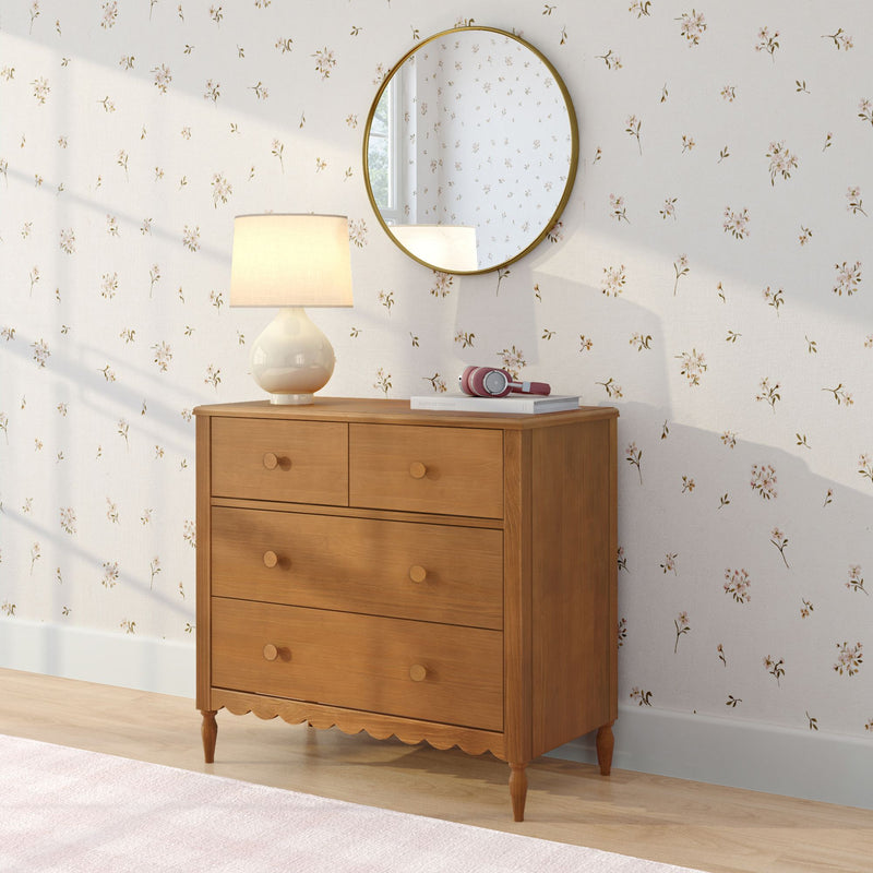 Wooden dresser with round brass mirror, ceramic table lamp and pink headphones on stacked books against white floral wallpaper, cozy bedroom decor