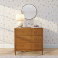 Wooden mid-century dresser with ceramic table lamp, round mirror and floral wallpaper, bedroom decor