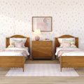 Twin girls bedroom with wooden beds, pink bedding and pillows, teddy bears, wooden dresser with lamp, floral wallpaper and framed poodle art