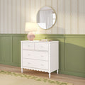 White four-drawer dresser with scalloped trim, pink table lamp and round mirror on green wainscoting under floral striped wallpaper