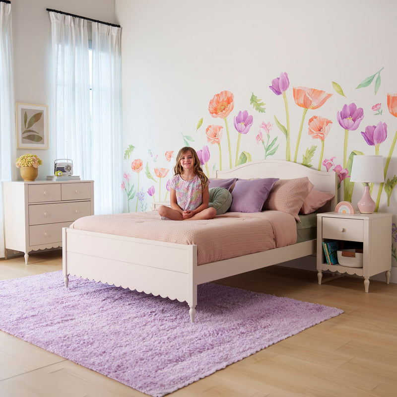 Girls bedroom decor with white wooden bed, pastel pink bedding, lavender rug, floral watercolor wall decals and smiling young girl