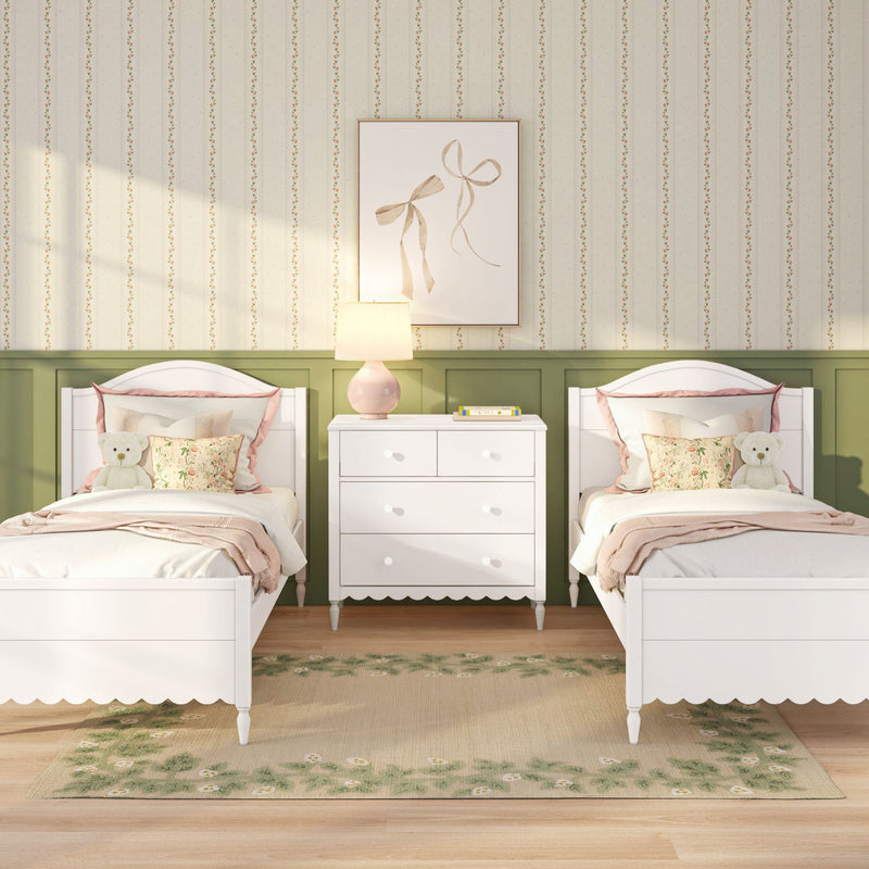 Children's twin bedroom with white wooden beds, pink floral pillows and teddy bears, white dresser with pink lamp, green wainscoting and floral area rug