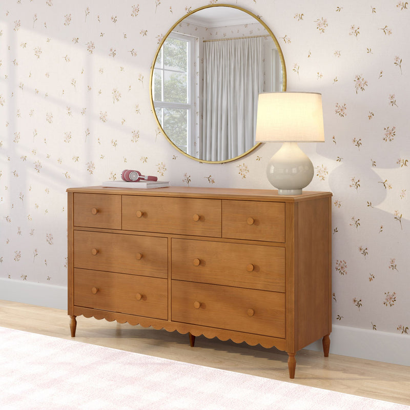Mid-century six-drawer wooden dresser with ceramic table lamp and round gold mirror over floral wallpaper, pink headphones on top