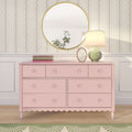 Pink vintage dresser with scalloped trim topped by a round gold mirror, green ceramic table lamp, stacked books and vertical floral wallpaper background