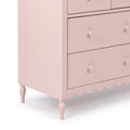 Light pink wooden dresser with four drawers, round knobs, scalloped base and turned legs for nursery or bedroom storage