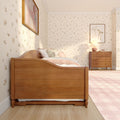 Cozy pink children's bedroom with wooden twin bed, floral wallpaper, plush teddy bear, wooden dresser and bedside lamp