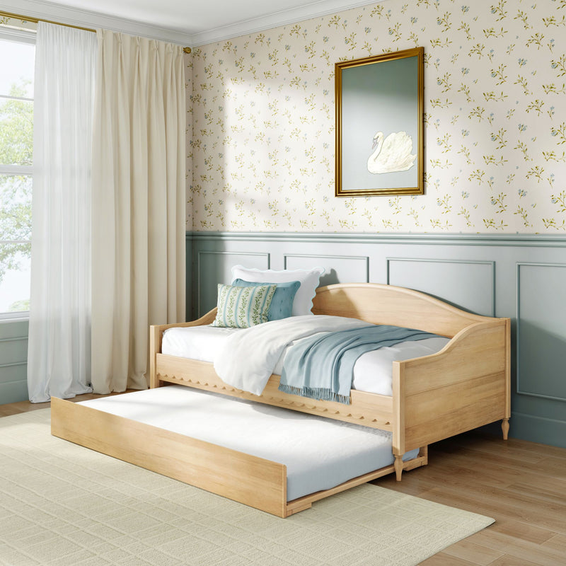 Wooden trundle daybed in a light-filled pastel bedroom with floral wallpaper, mint wainscoting, gold-framed swan print, cream curtains and blue throw